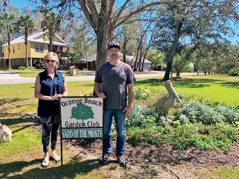 Ricky Deblieux and Susan Grant standing beside an Orange Beach Garden Club Yard of the Month sign in March 2021