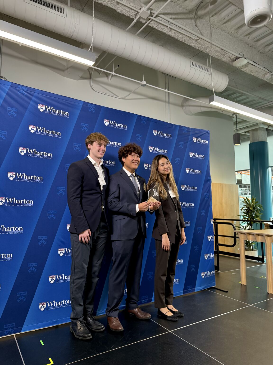 The three-person SphereUs founding team posing at a Wharton event with an award