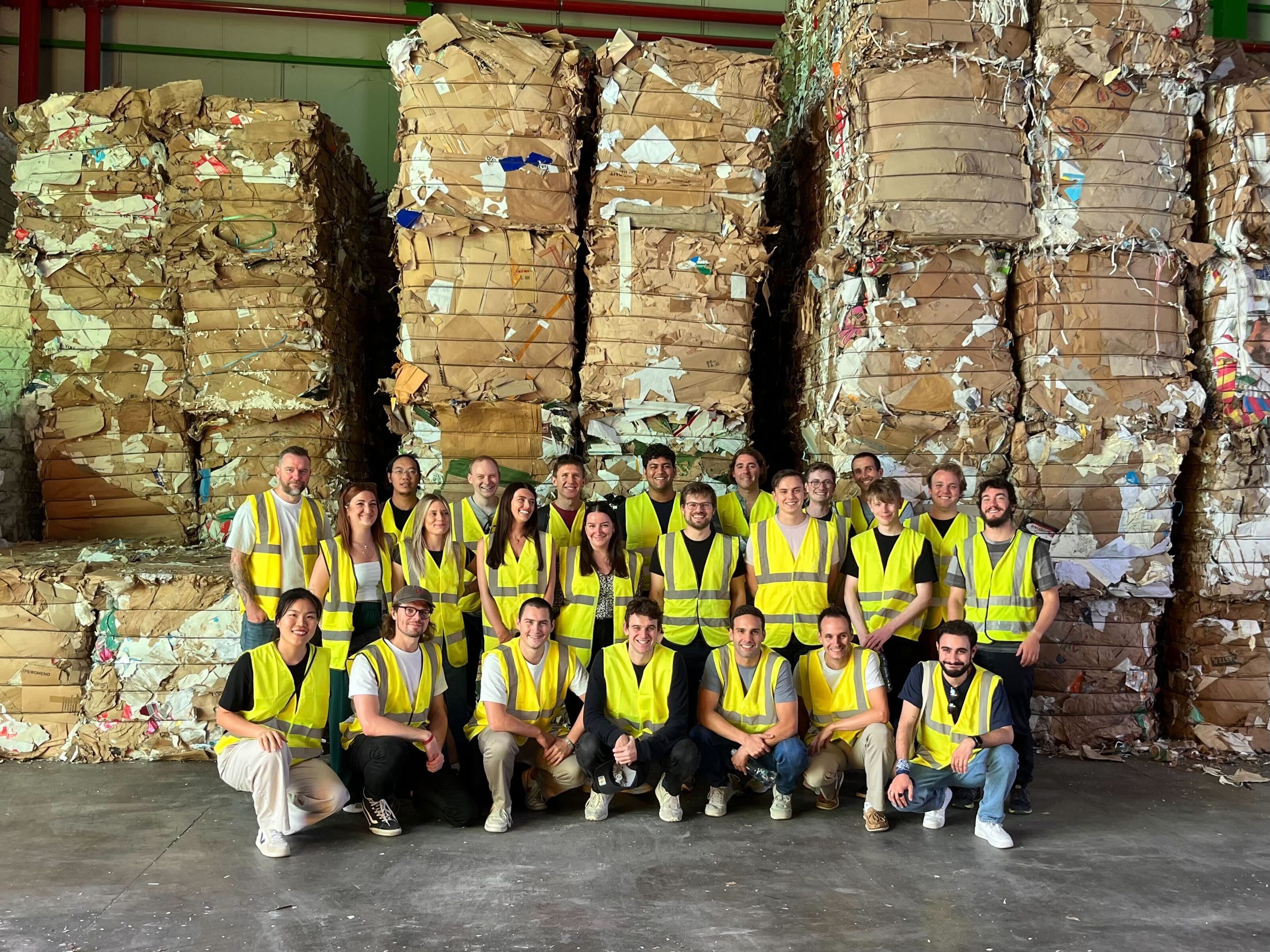 The Safi team wearing high-visibility vests in front of tall stacks of baled cardboard