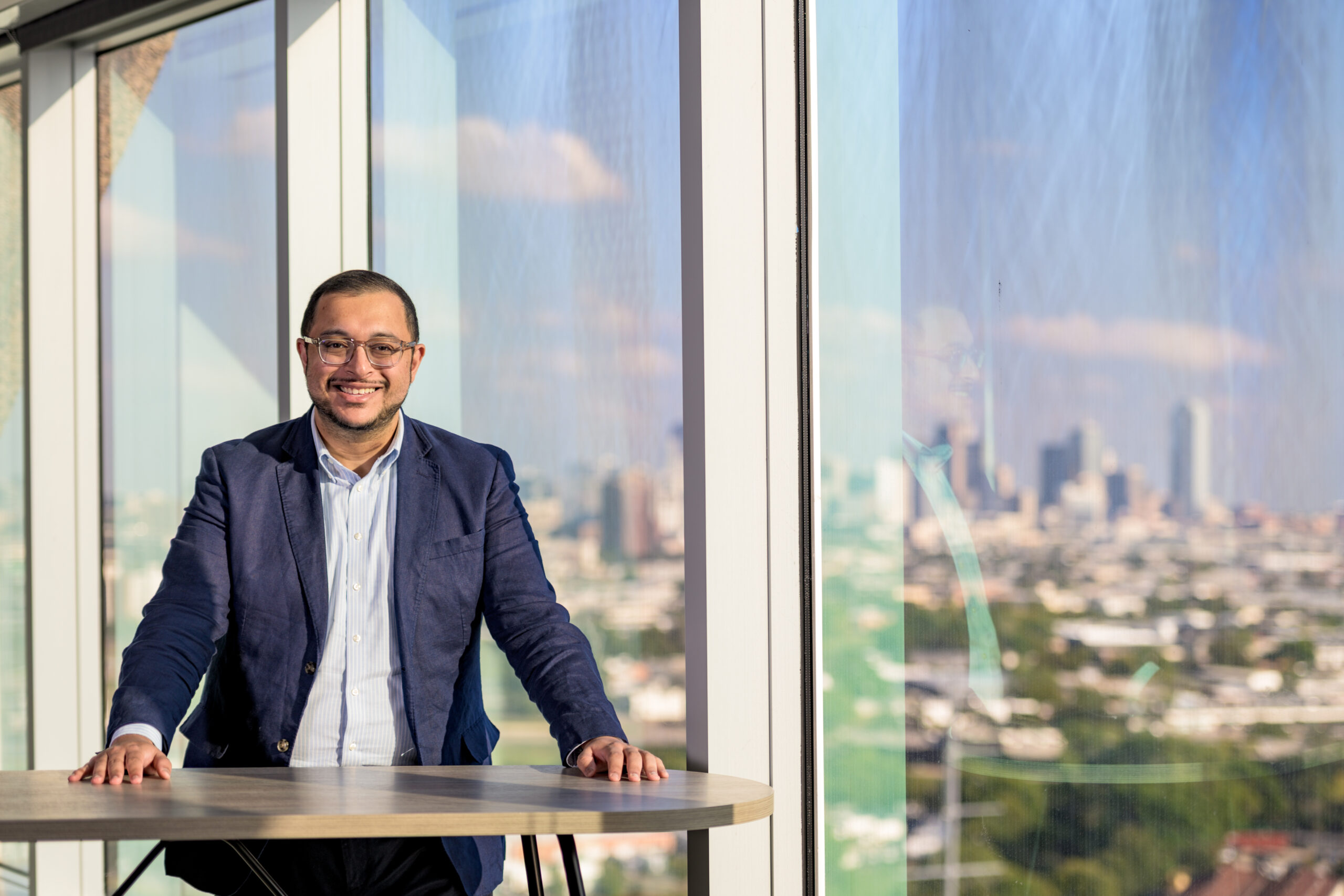 Ritish Patnaik standing at a table beside windows overlooking Dallas