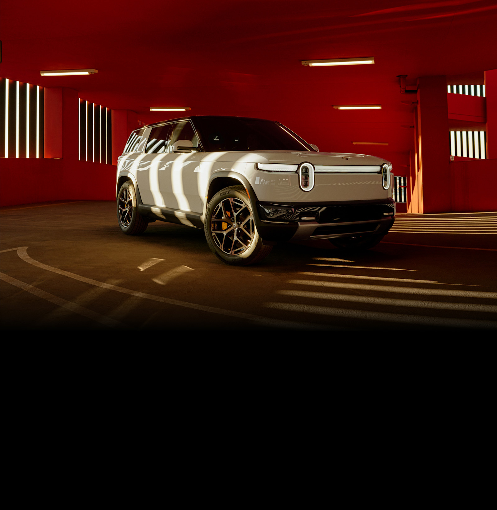 White Rivian R2 SUV photographed inside a red architectural space