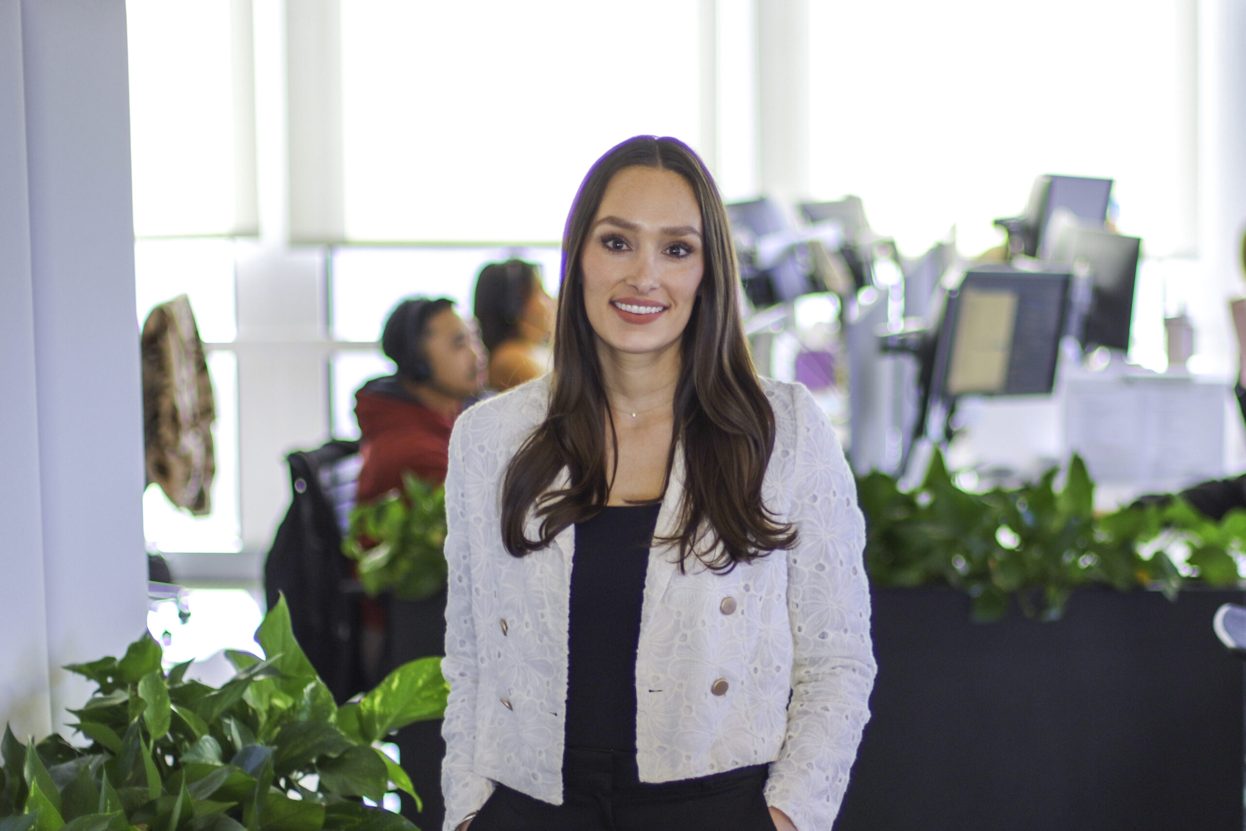 A person in RIVO's bright office, with coworkers, monitors and planted workstation dividers behind her