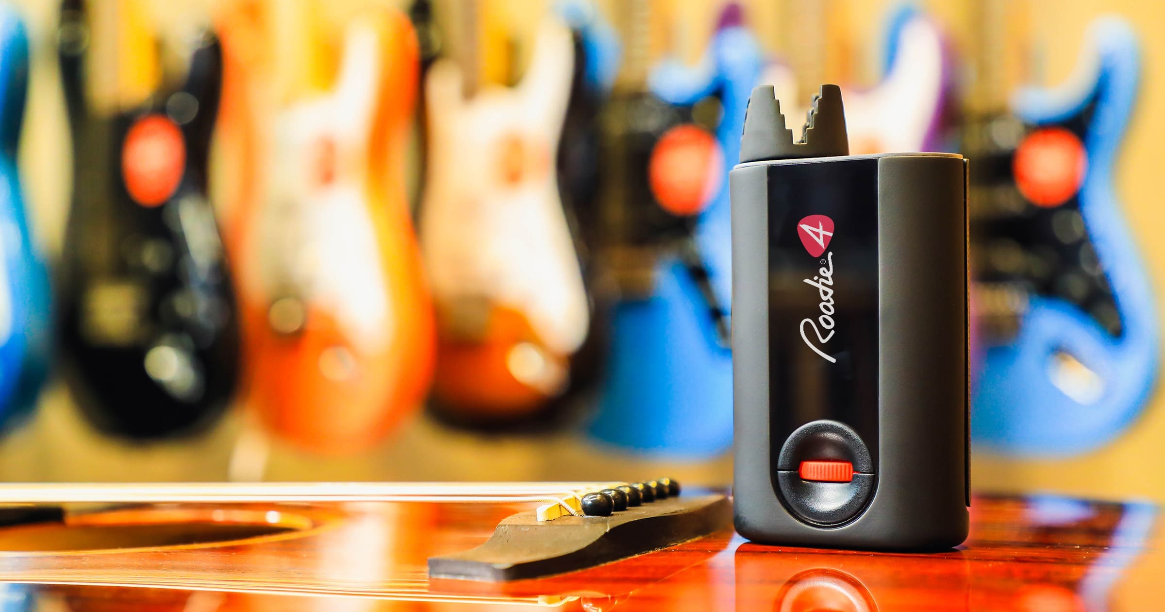 A Roadie automatic tuner standing on a guitar with colorful instruments behind it