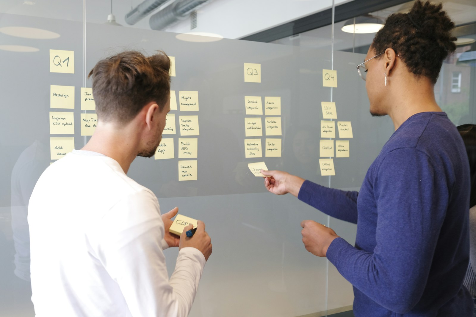 Two product teammates arranging quarterly roadmap notes on a glass wall