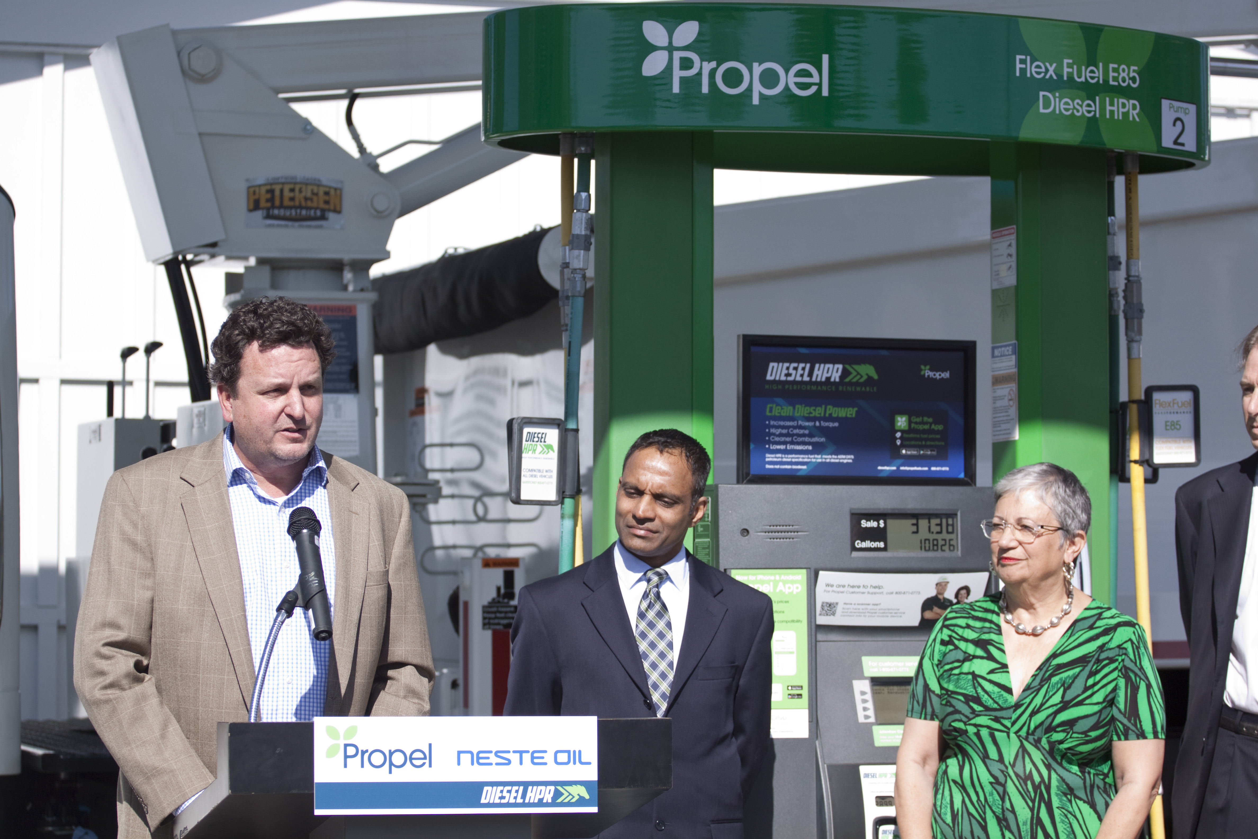 Rob Elam speaks beside a green Propel fuel pump at the 2015 Diesel HPR launch in Sacramento, with Neville Fernandes and Mary Nichols nearby.