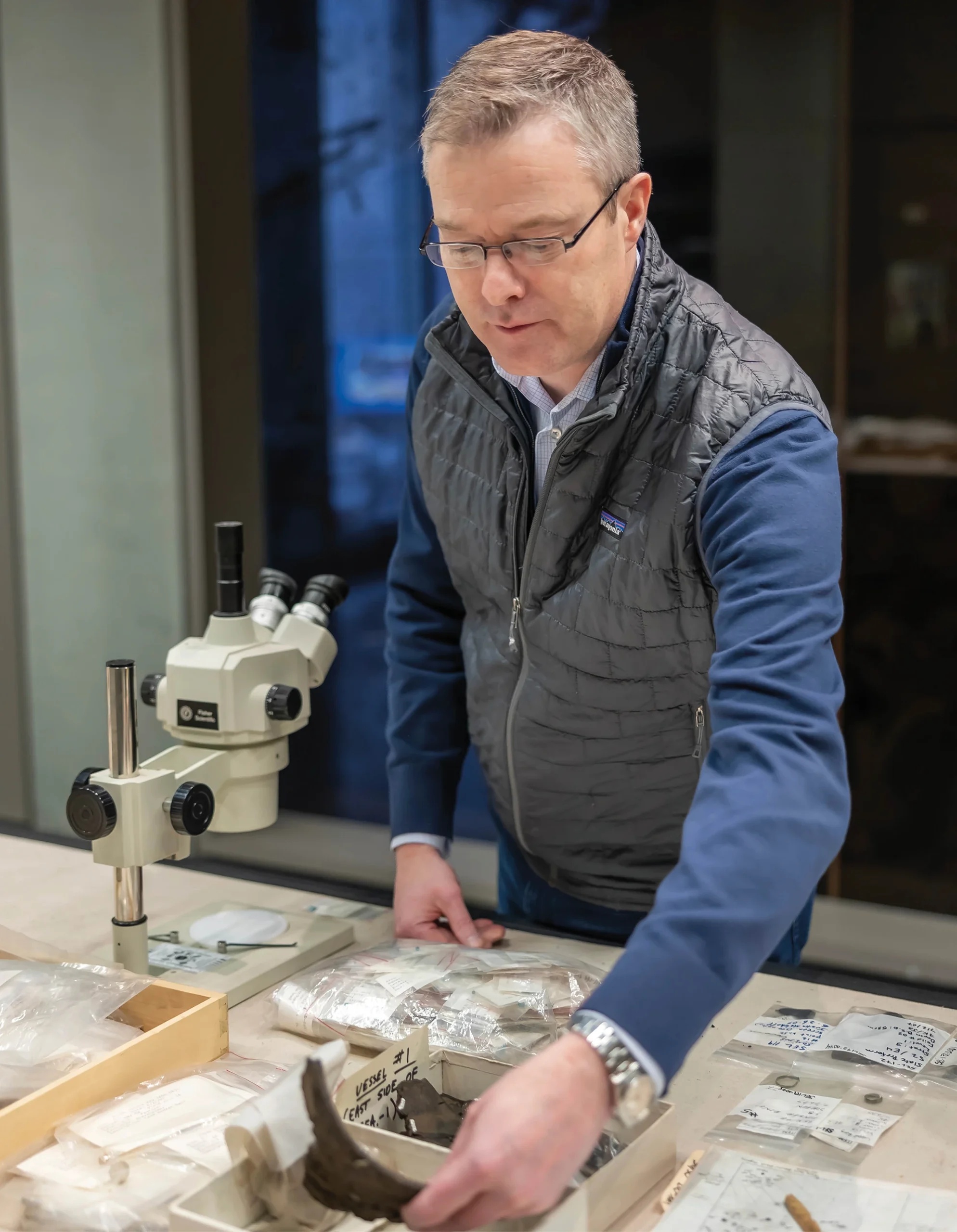 Rob Gillam examining archaeological material beside a microscope at the Anchorage Museum