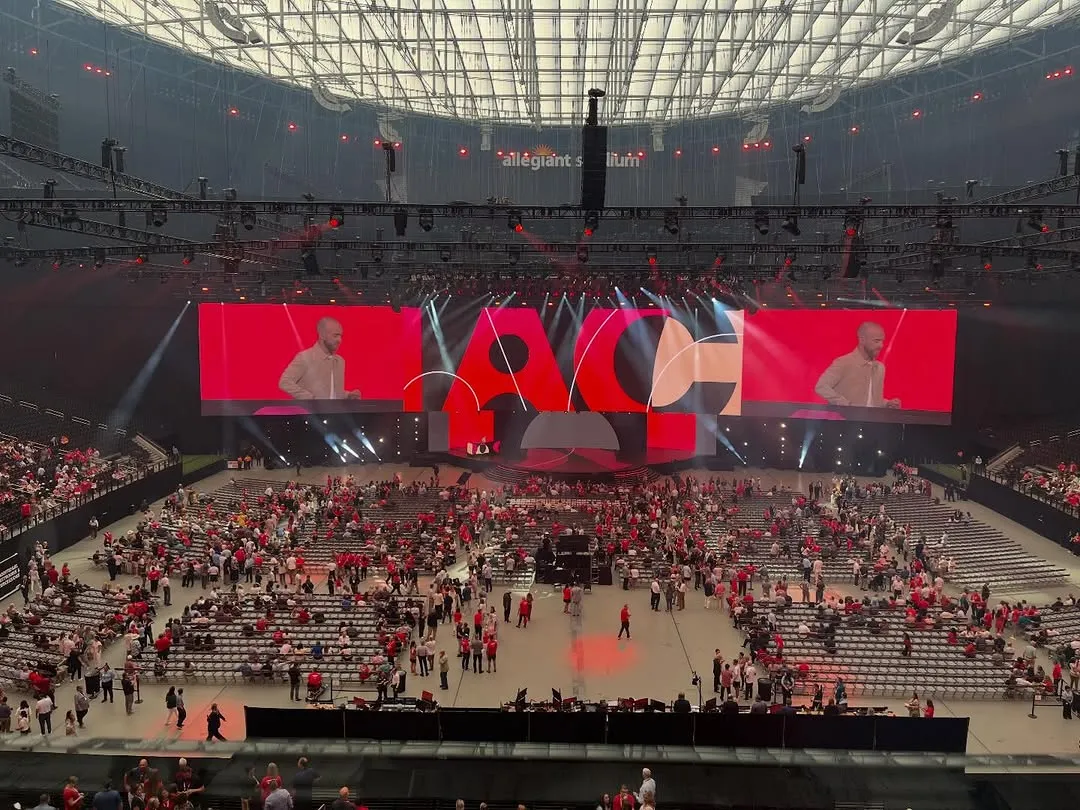 A corporate stadium production with large stage screens and an audience seated around the stage