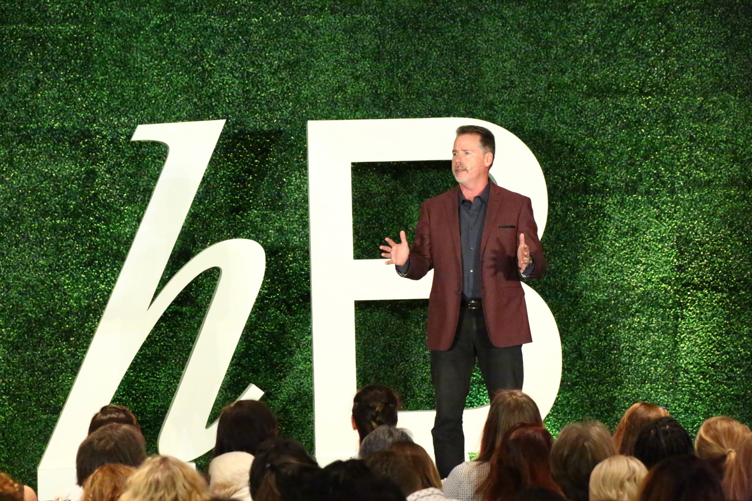 Rob Kosberg in a burgundy jacket speaking onstage to a seated audience