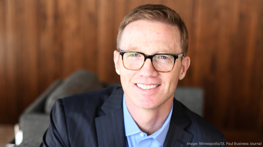 Rob Nelson seated in an office, wearing glasses and a dark suit