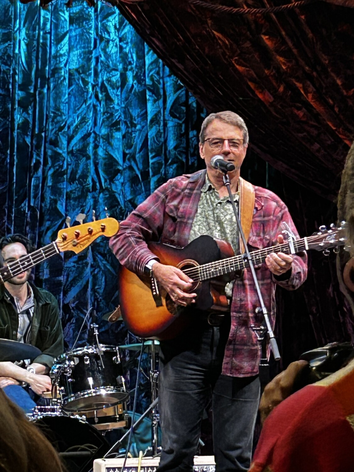 Robert Berkeley playing acoustic guitar and singing onstage in Nashville, with musicians behind him.