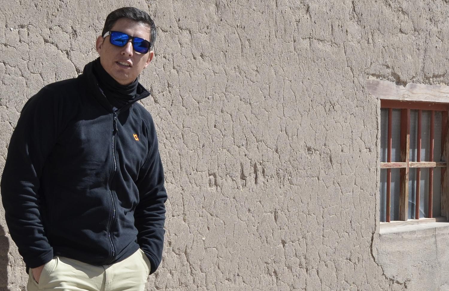 Robert Bestwick standing beside a textured adobe wall in bright sunlight