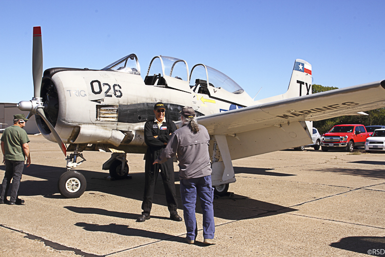 A Trojan Phlyers T-28 on an airfield, with a pilot talking to a visitor beside its wing