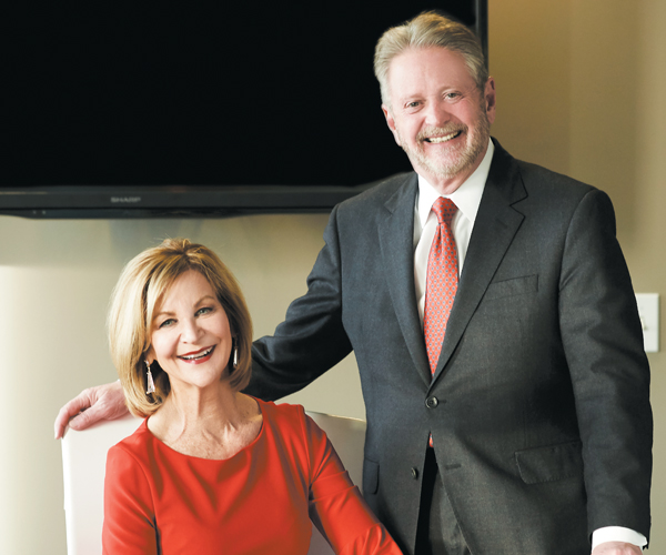 Kathryn Falls seated beside Robert Falls, who is standing in a suit