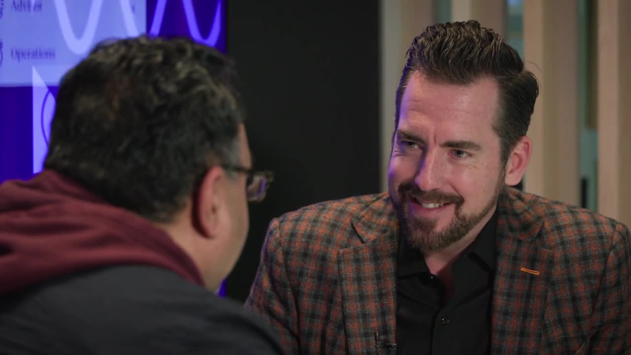 Robert Sofia in a checked jacket, speaking with interviewer Suleman Din
