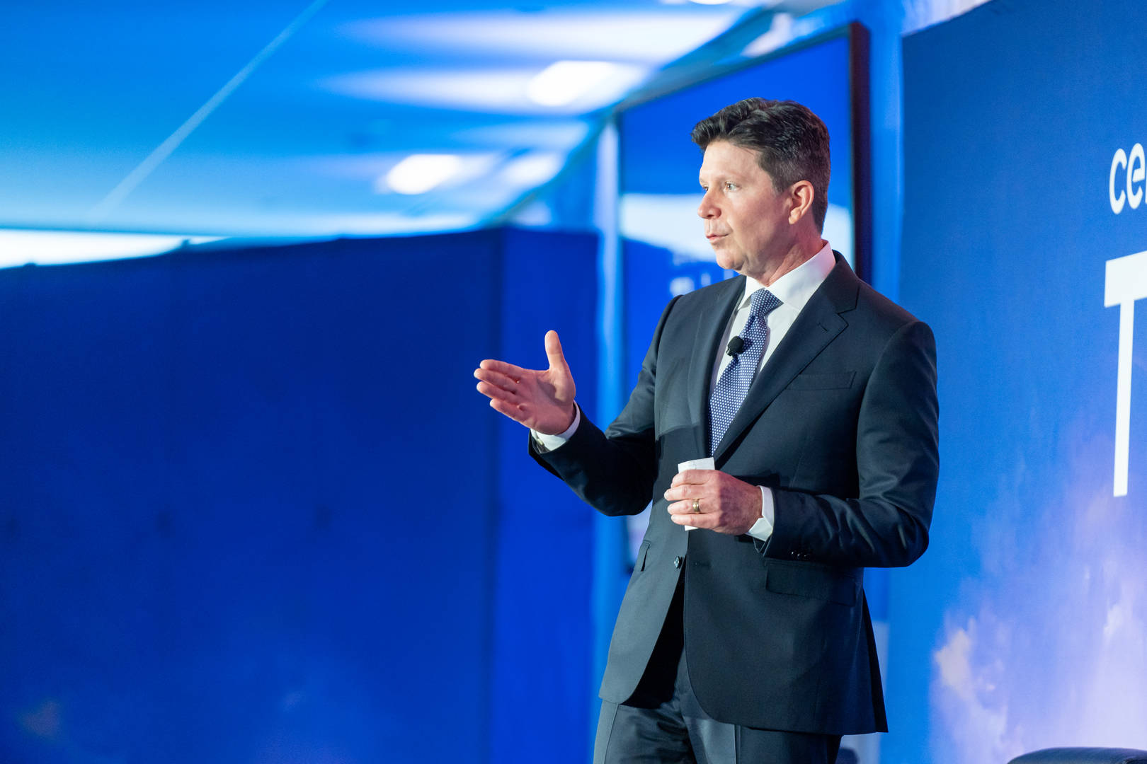 Robert Mauch addressing an audience against a blue conference backdrop