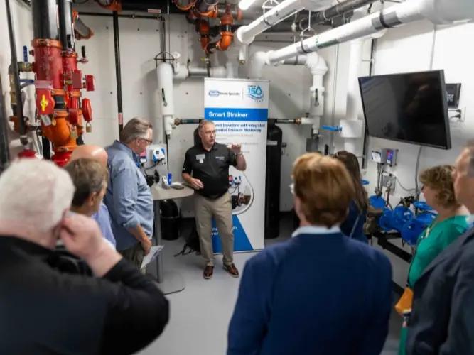 Visitors watching a product demonstration among pipes and equipment during Watts’ anniversary tour