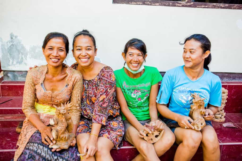 Four NOVICA artisans sitting together and holding carved wooden figures