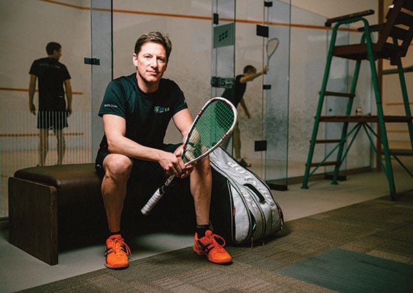 Roger Hardy holding a squash racket beside the court at Hollyburn Country Club