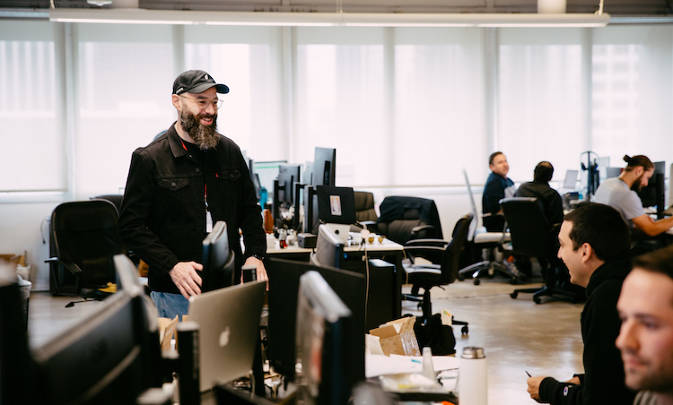 Roger Volodarsky talking with colleagues among desks and computer monitors at Puffco