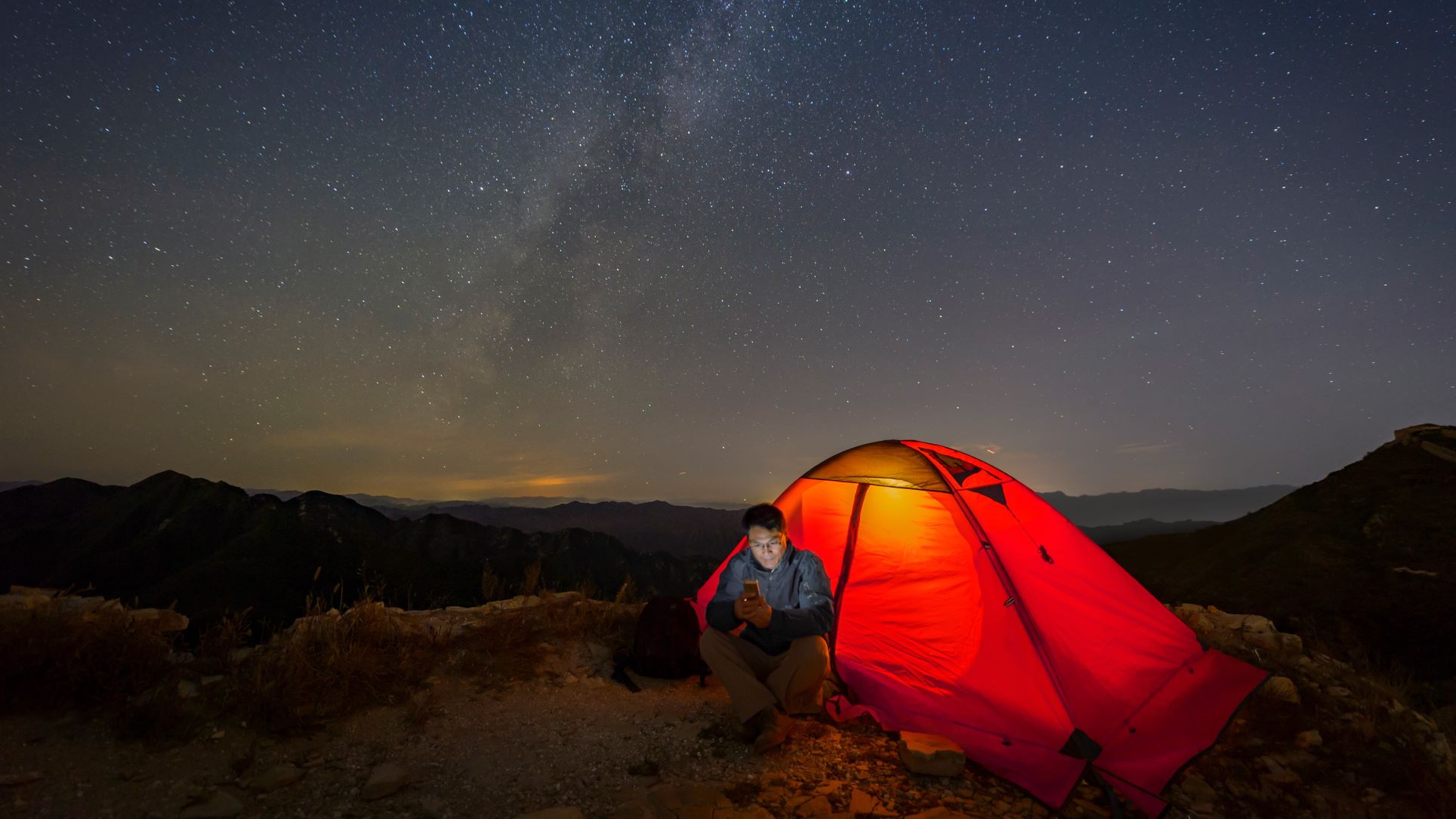 A camper beneath a star-filled Canadian sky using a mobile phone where Rogers Satellite is designed to work