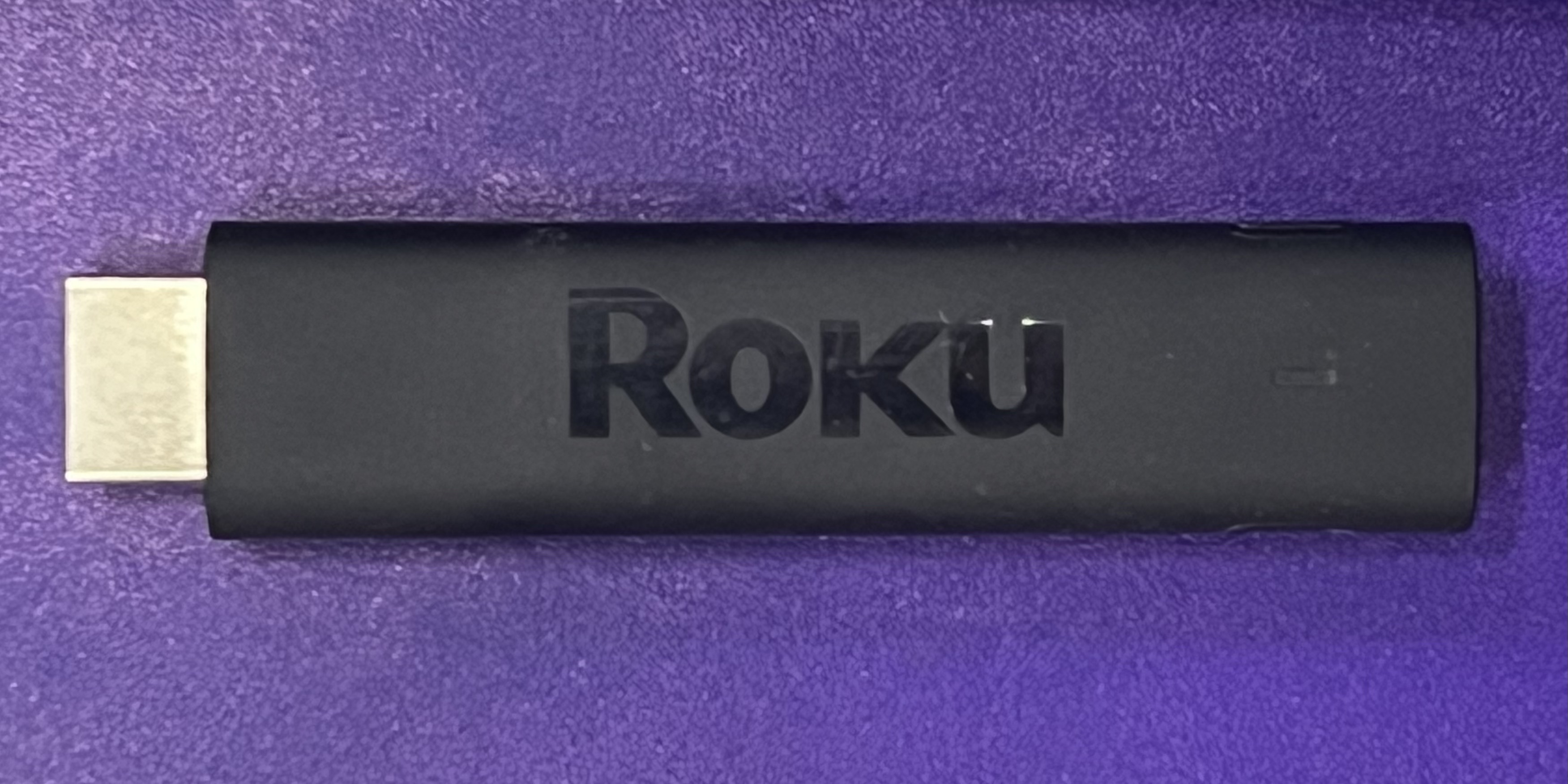 A Roku Streaming Stick 4K and purple Roku remote on a dark surface