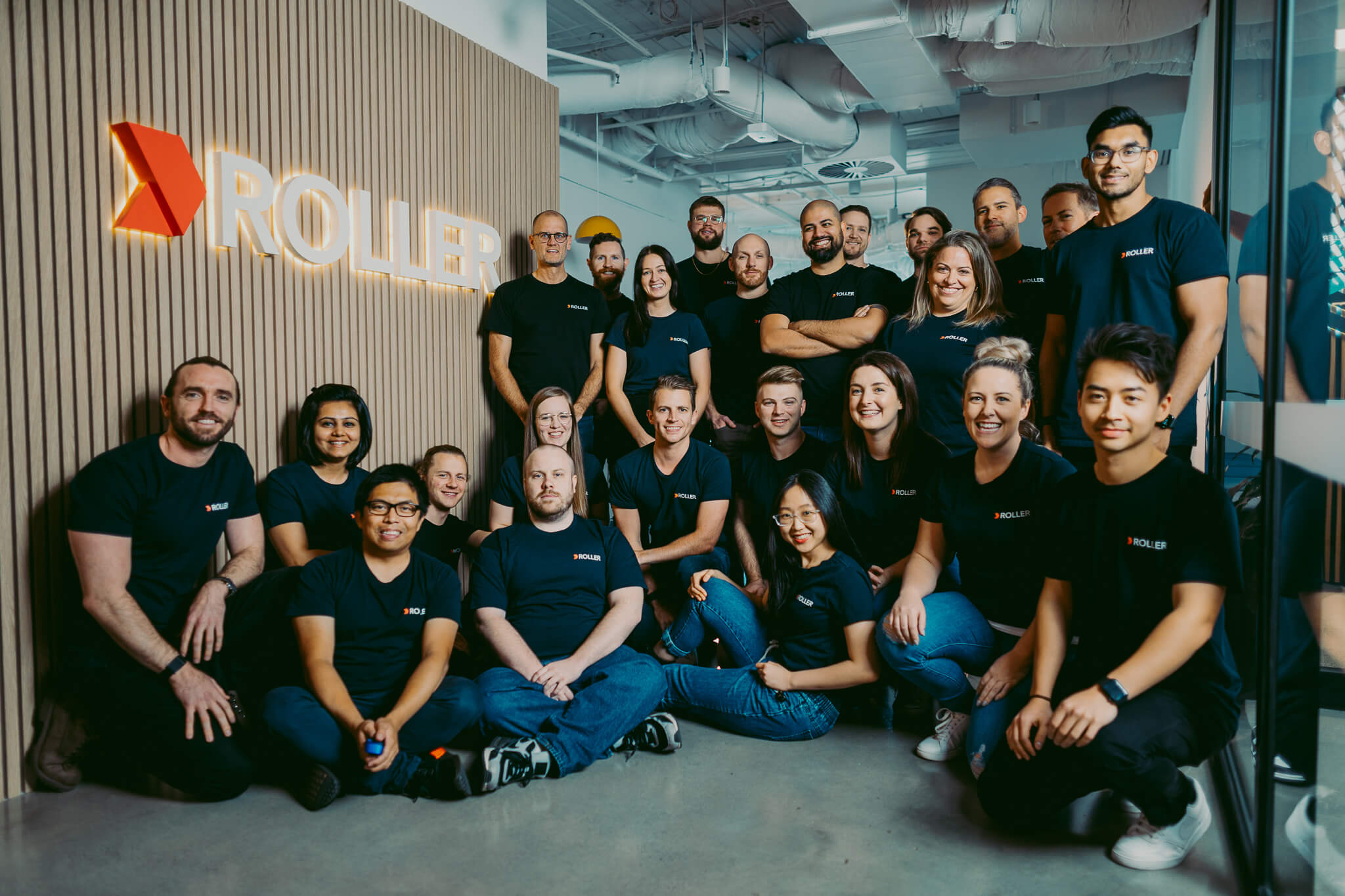 Members of the ROLLER team gathered beside the company sign in an office