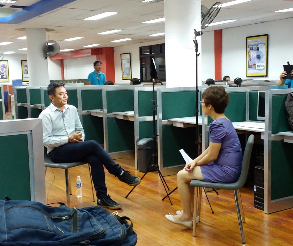 Rom Agustin seated opposite Money Mind host Chor Khieng Yuit among Callbox office cubicles