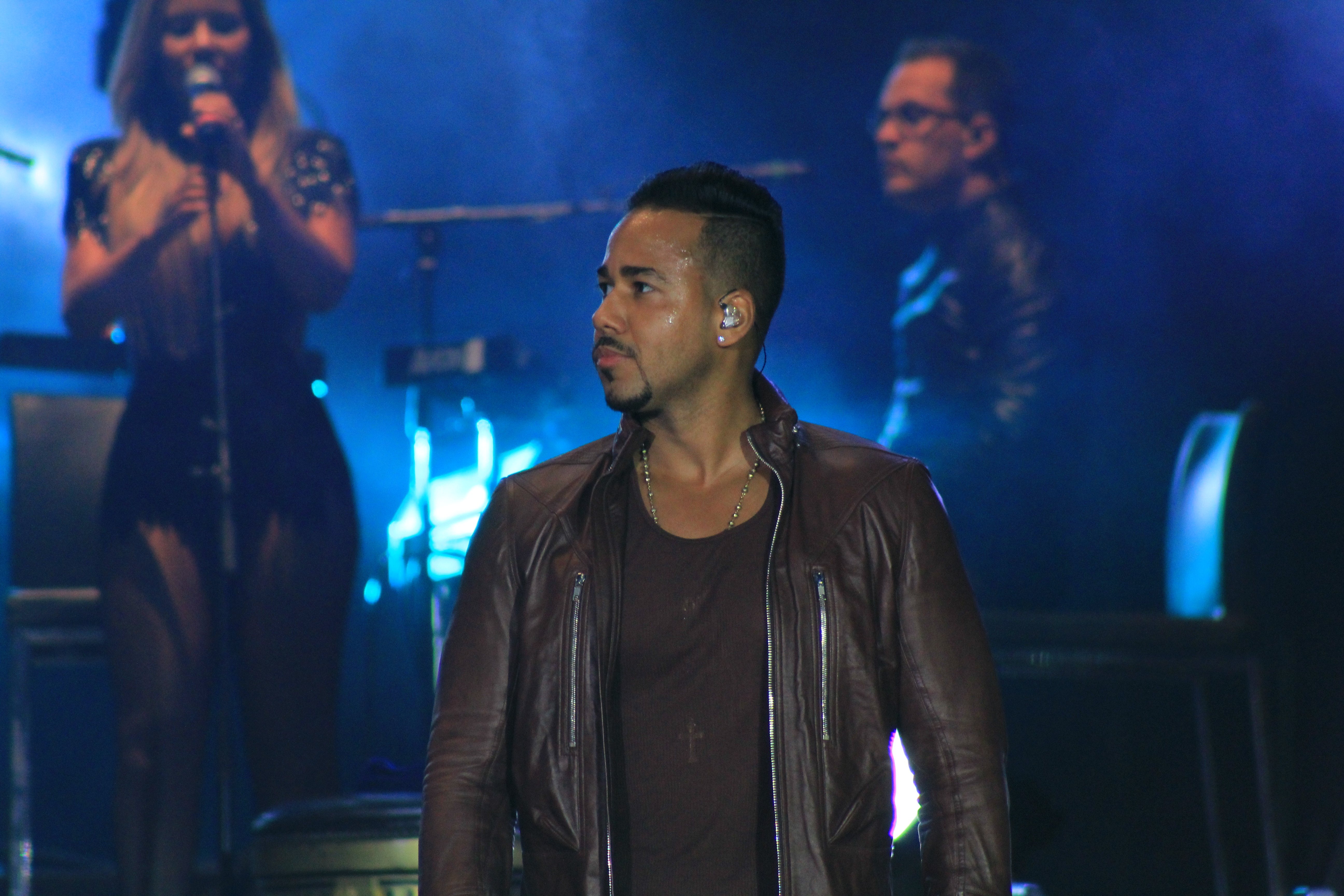 Romeo Santos pauses onstage under blue concert lights at the Estadio Nacional de Chile in 2015