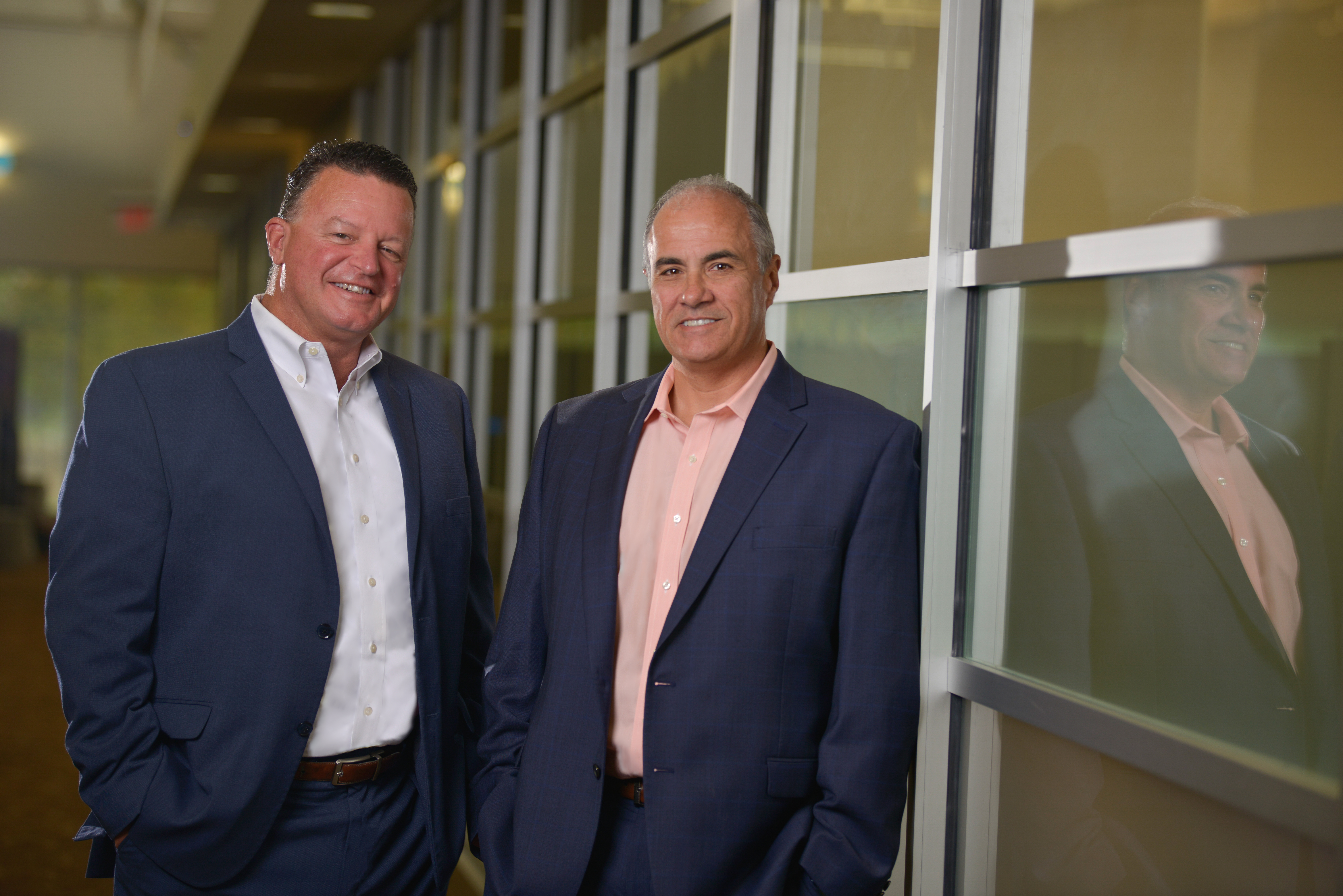 Ken Scaturro, left, and Ron Gaboury, right, standing beside office windows.