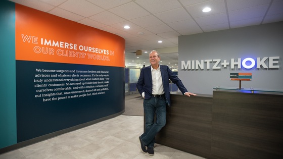 Ron Perine standing in the Mintz + Hoke office beside a wall describing the agency's immersive approach