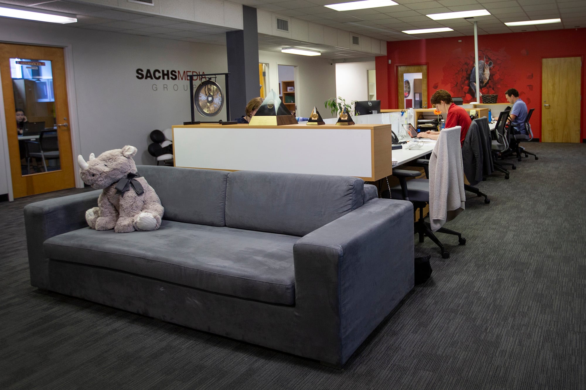 Sachs Media's open office, with staff at desks, awards and a plush rhinoceros on a sofa