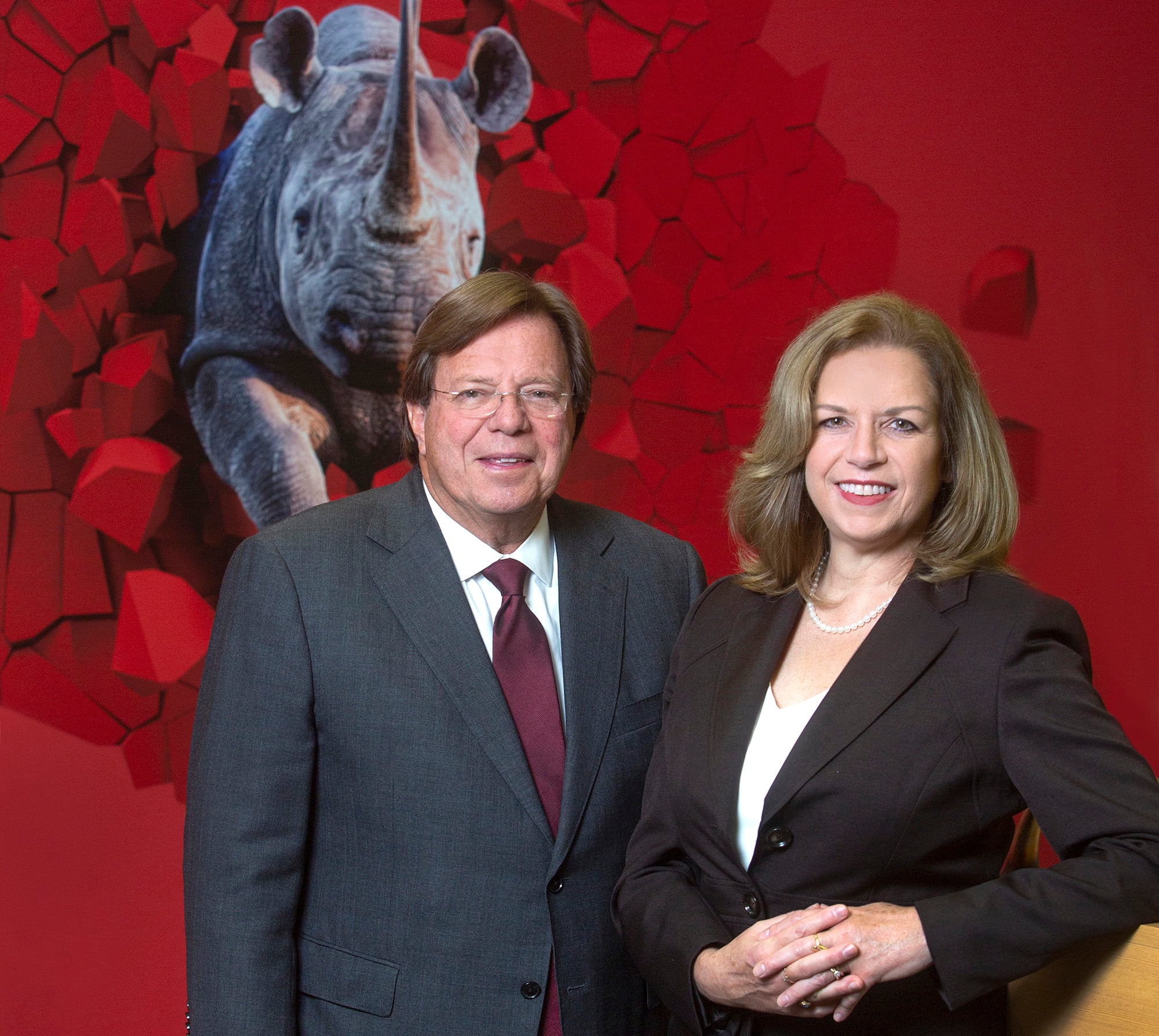 Ron Sachs and Michelle Ubben standing together in front of a red wall and rhinoceros mural