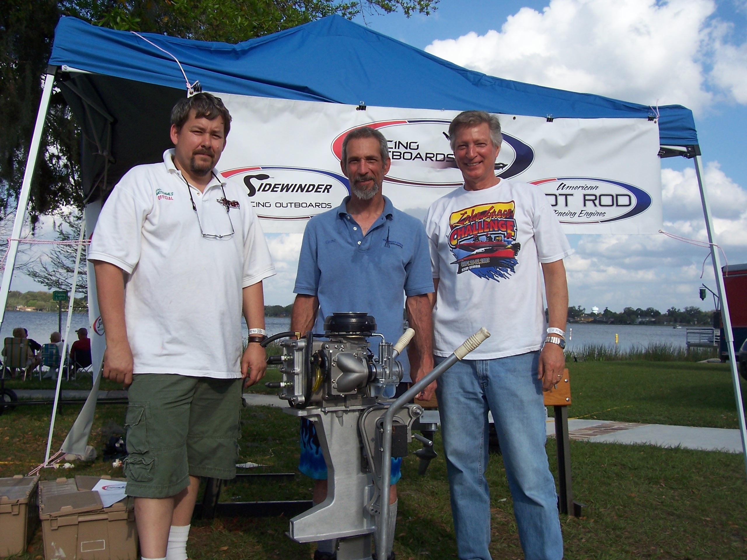 Ed Runne, Gene Schertz and Ron Selewach stand beside a Sidewinder outboard engine at a racing event