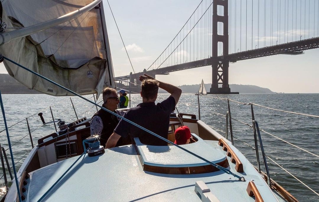 Sailors aboard a wooden boat on San Francisco Bay with the Golden Gate Bridge ahead.
