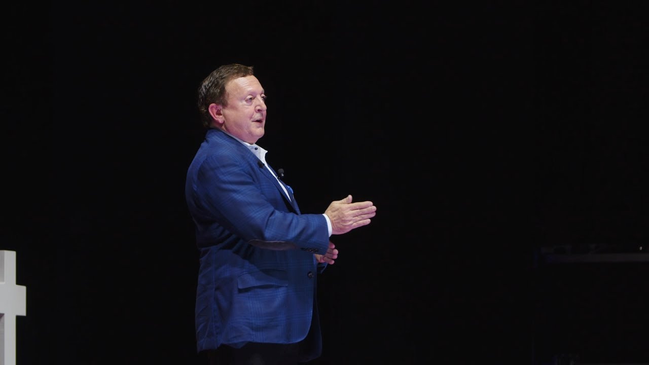 Ronald Diamond speaking onstage at TEDxDavenport in a blue suit