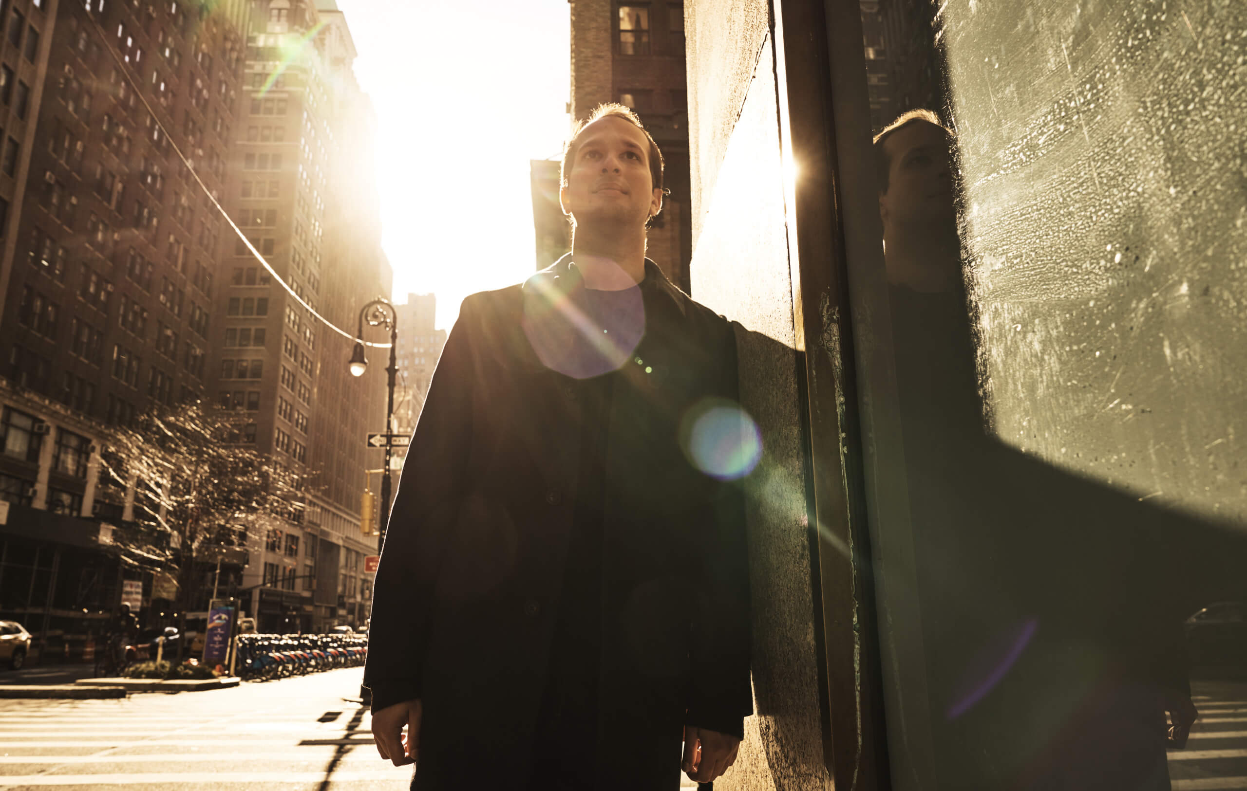 Roneil Rumburg standing beside a reflective window on a sunlit city street