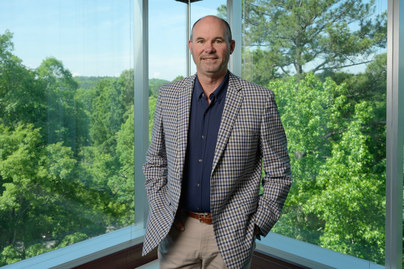Ronnie Pruitt standing beside tall windows overlooking green trees