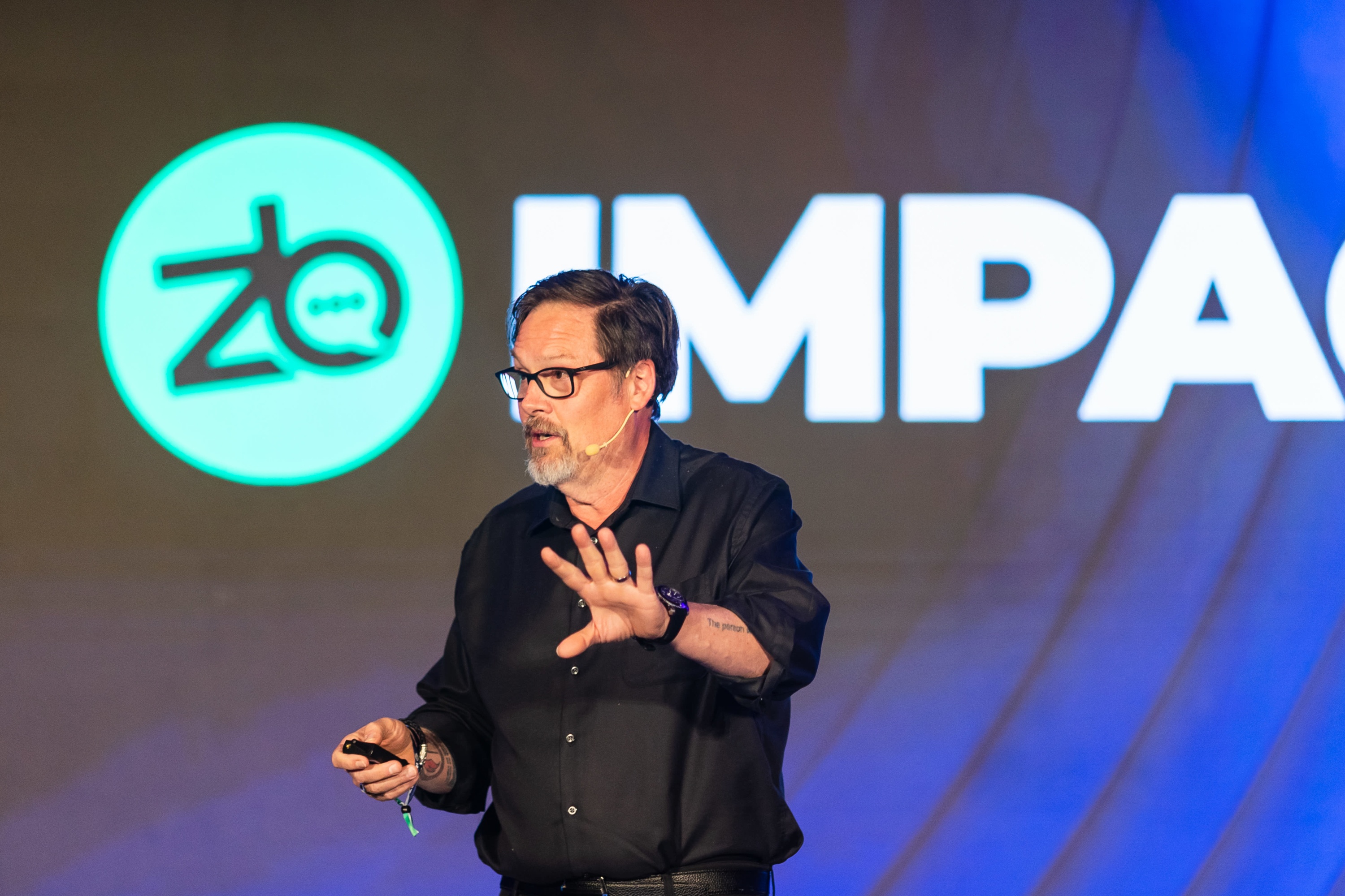 Ross Buhrdorf speaking onstage, wearing a headset microphone and holding a presentation remote
