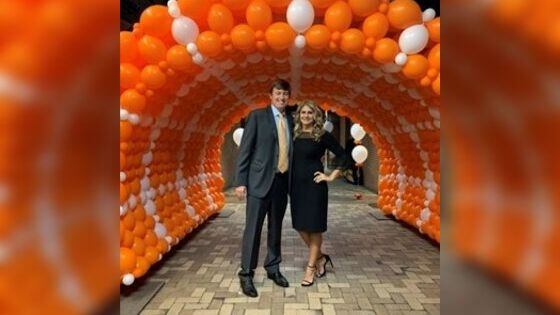 Ross and Sara Croley standing beneath an arch of orange and white balloons