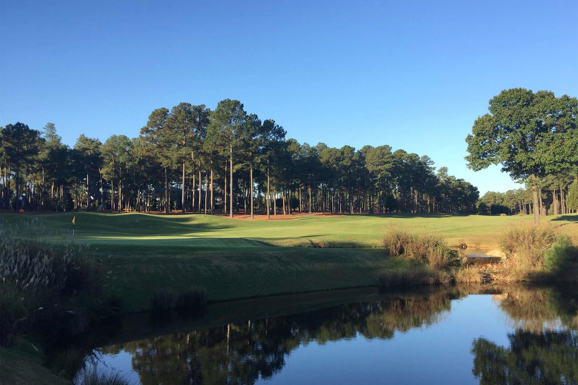 Pinewild Country Club golf course bordered by pine trees, with water in the foreground
