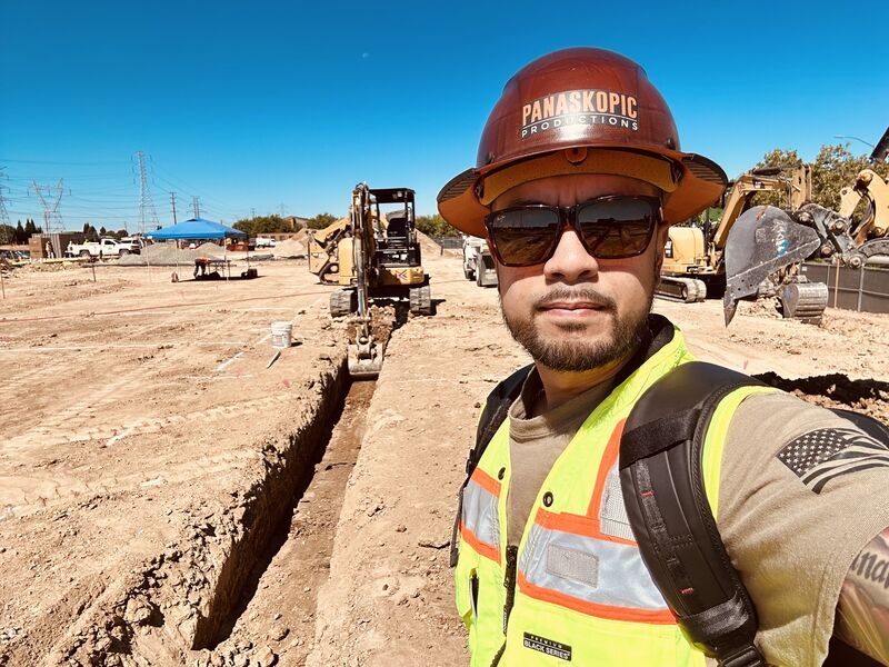 Roy Panaligan in a hard hat and high-visibility vest beside a trench and construction equipment