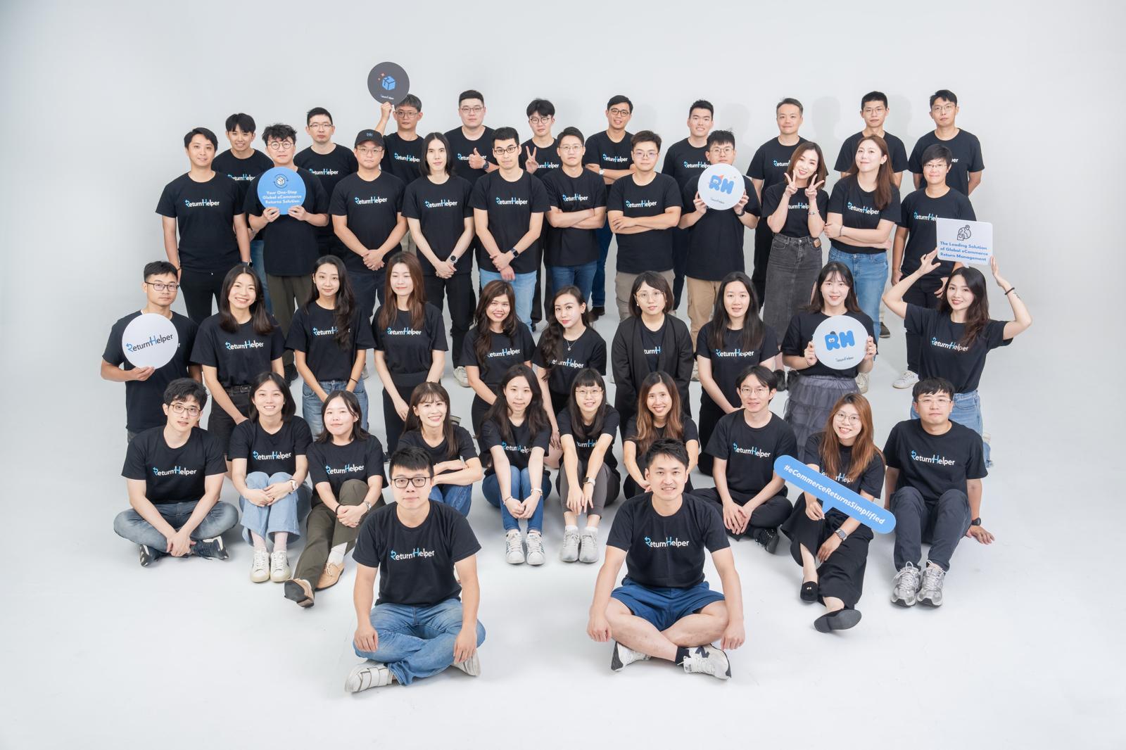 Return Helper colleagues pose together in matching dark company shirts, with several holding signs.