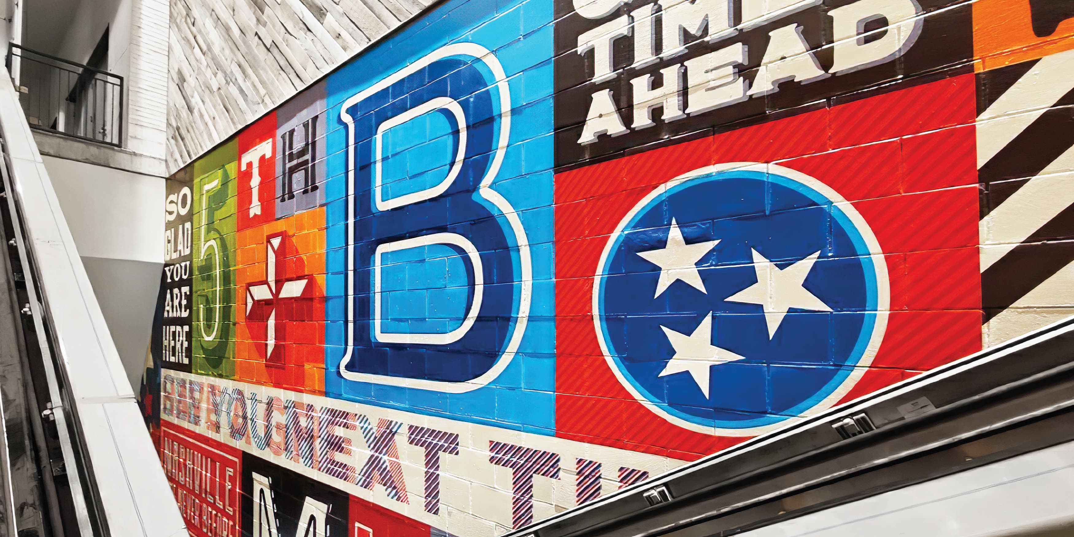 Colorful letterpress-inspired Fifth + Broadway mural beside an escalator in Nashville