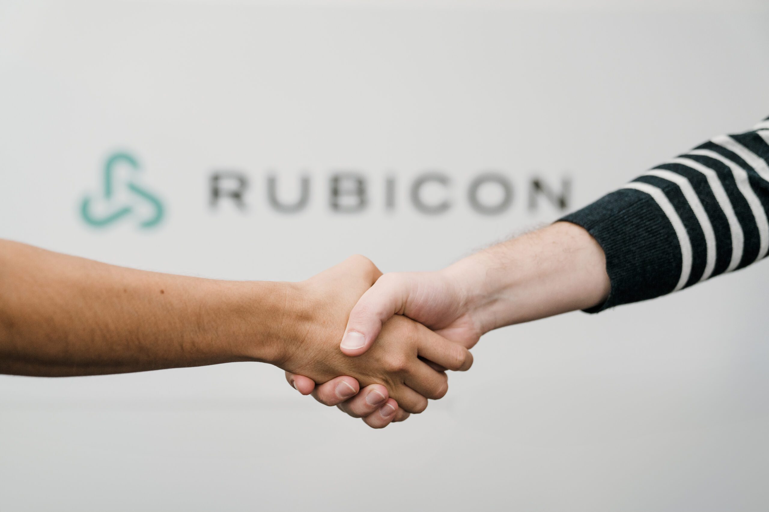 Two people shake hands in front of a Rubicon sign