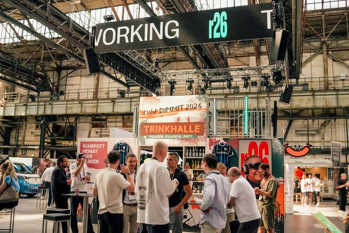 Festival visitors talking around tables beneath the industrial roof of the Jahrhunderthalle