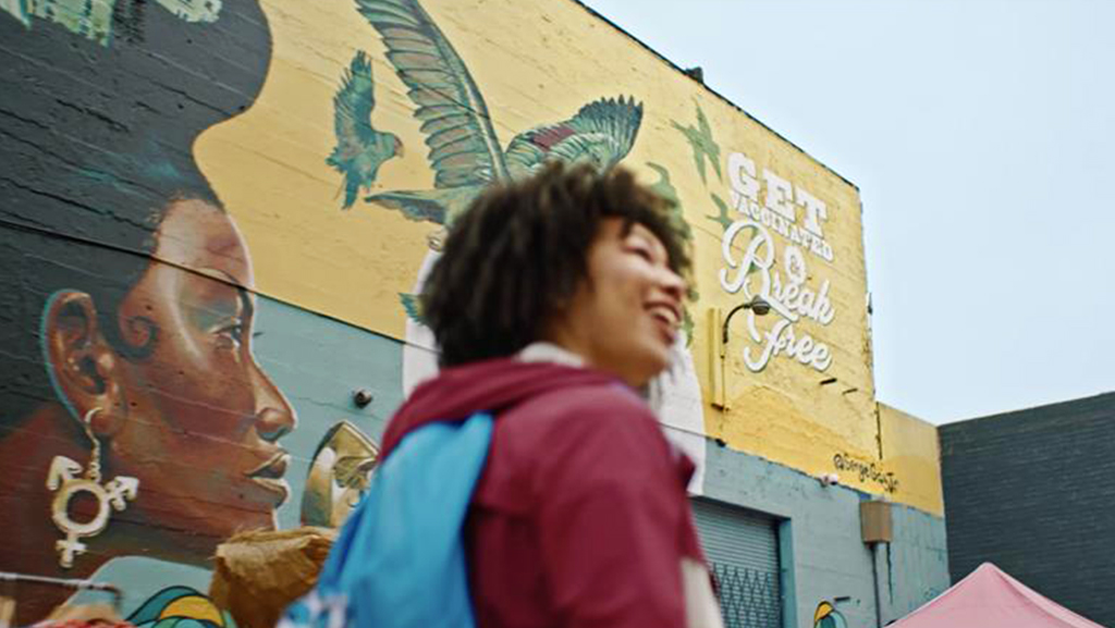 A young person walks past a colorful California COVID-19 campaign mural encouraging vaccination and freedom