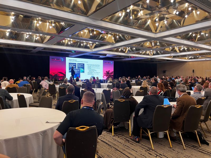 Audience seated at round tables facing the stage during Rupert Morrison’s OPEX Week presentation