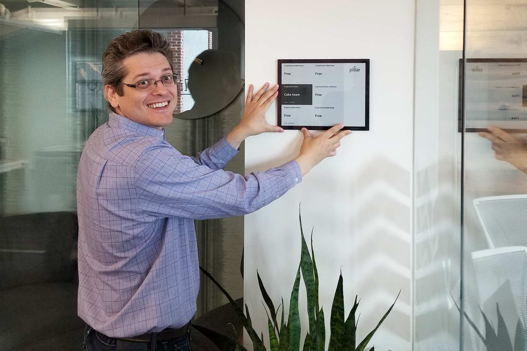 Russ Wilcox gestures toward a Joan electronic paper room display in an office.