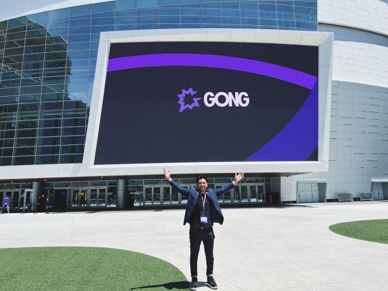 Russell Banzon standing outside a venue beneath a large Gong sign with both arms raised
