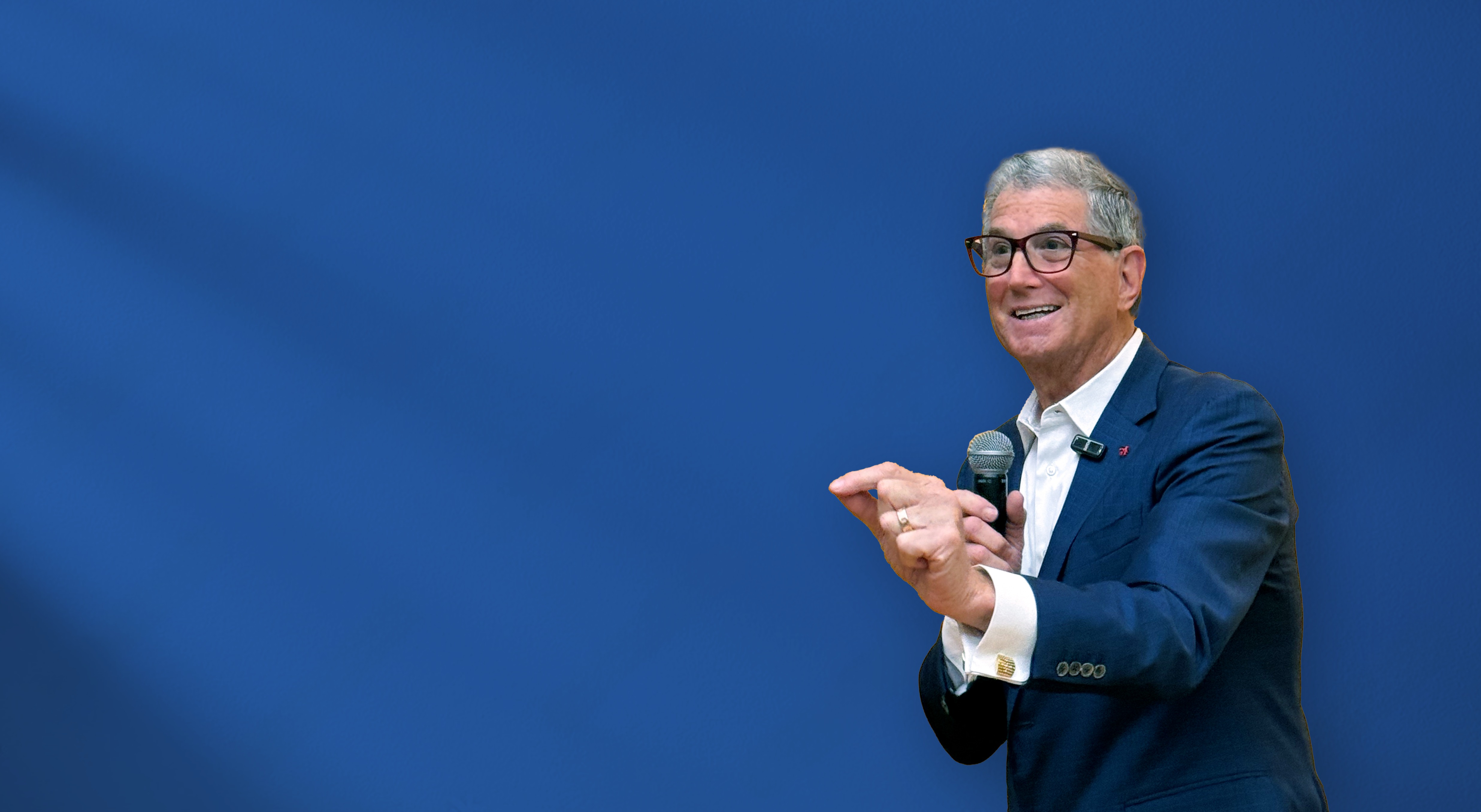 Russell Kern speaking with a handheld microphone against a blue background